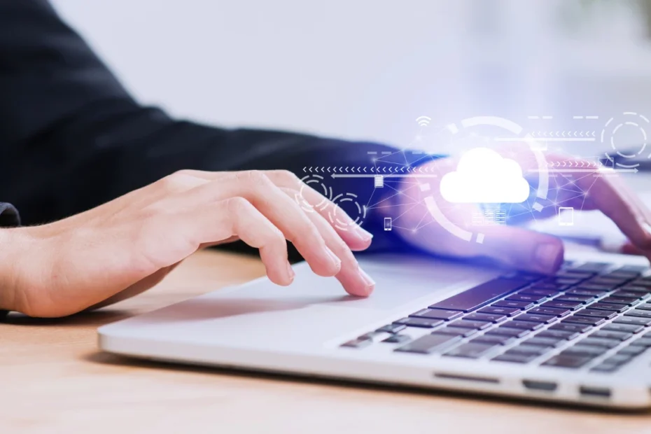Computação em nuvem para pequenas empresas: Guia prático de migração — mãos usando um notebook em ambiente corporativo com ícone de nuvem e elementos digitais de tecnologia ao fundo.